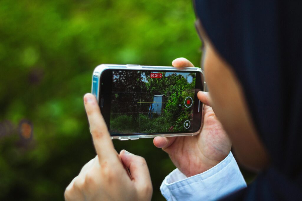 pexels photo 33928939 33928939 Close-up of person using smartphone to film a green outdoor scene in daylight.